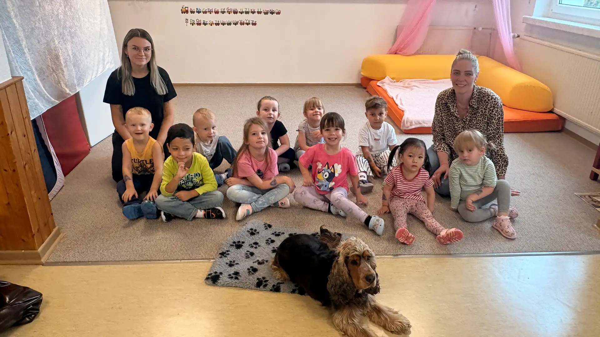 Robby, ein Besuchshund, sitzt mit Kindern aus der Kita Sonnenschein und gemeinsam lernen sie Rücksichtnahme, Vertrauen und ein respektvolles Miteinander.