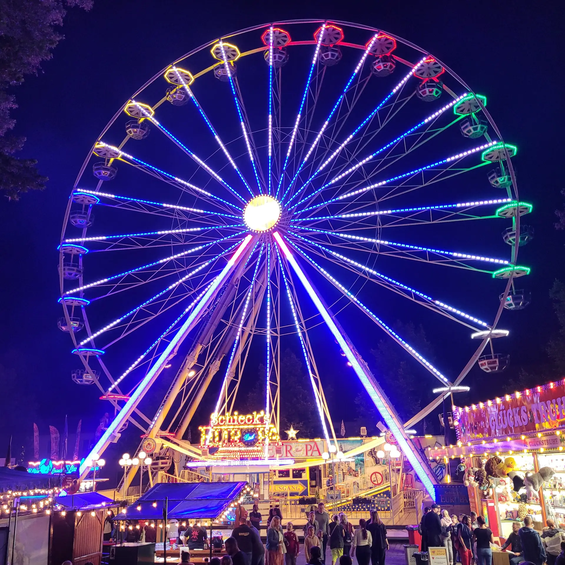 Riesenrad auf dem Festgelände mit Menschen im Vordergrund
