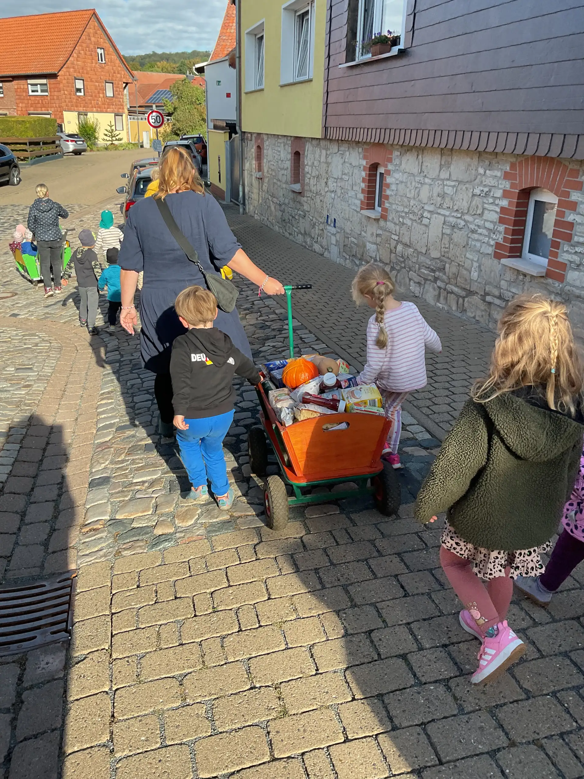 Kinder mit einem Bollerwagen voller Erntegaben auf dem Weg zum Erntedank-Gottesdienst.